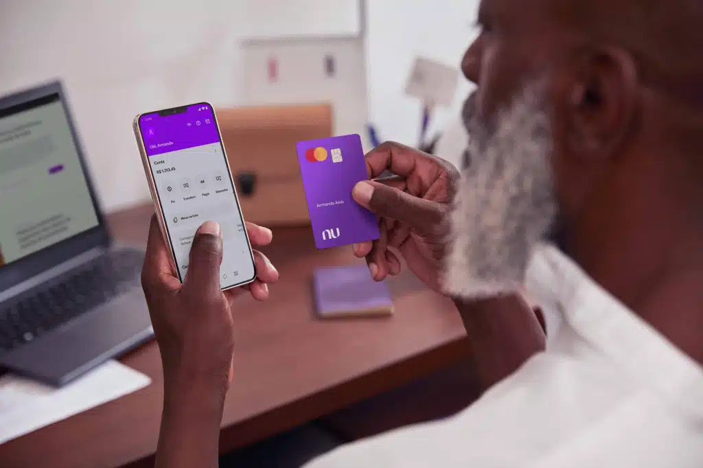 homem consultando aplicativo nubank no celular e segurando cartao de credito